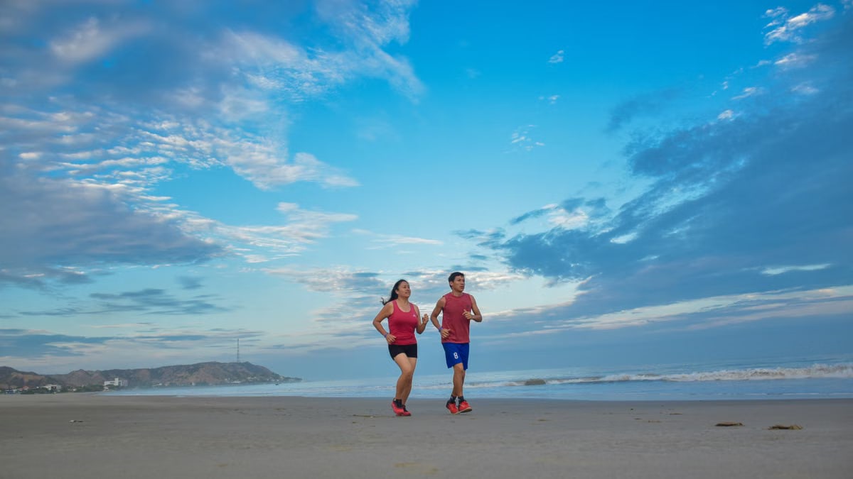 A couple enjoys jogging together along a scenic beach under a bright blue sky.